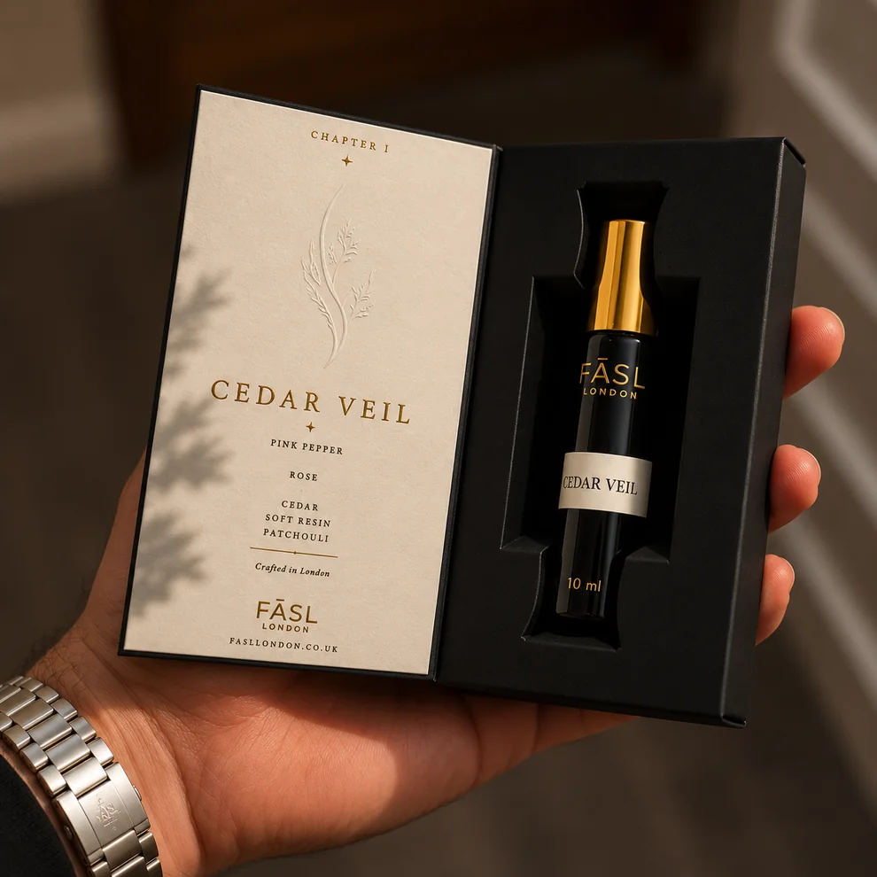 A hand holding the open FĀSL presentation box for Chapter I · Cedar Veil, with the fragrance notes card and the 10ml roll-on vial inside